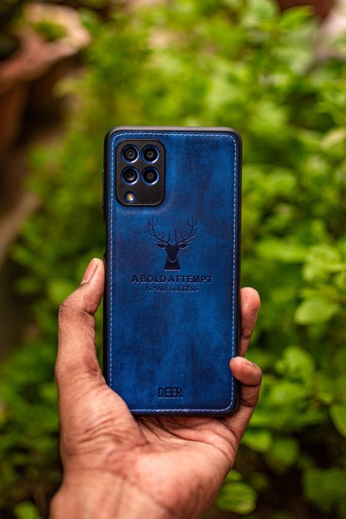 A hand holding a smartphone with a blue case featuring a bold design, set against a blurred green background.