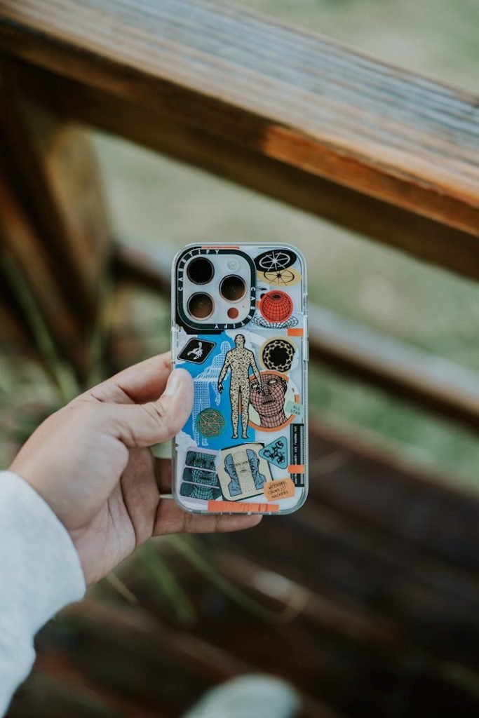 A close-up of a hand holding a creatively designed smartphone case outdoors, featuring various colorful elements.
